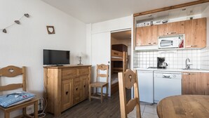 Une chambre compacte comprenant un bureau en bois, une télévision, un lit superposé, une kitchenette équipée d’un four à micro-ondes et un évier.