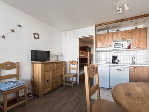 A compact room with a wooden desk, a television, a bunk bed, a kitchenette with a microwave, and a sink.