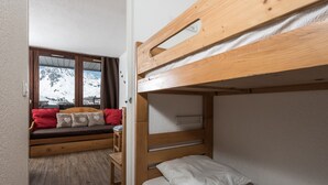 Une pièce avec un lit superposé, un banc en bois avec des coussins, une fenêtre donnant sur des montagnes enneigées et une porte menant à une autre pièce.