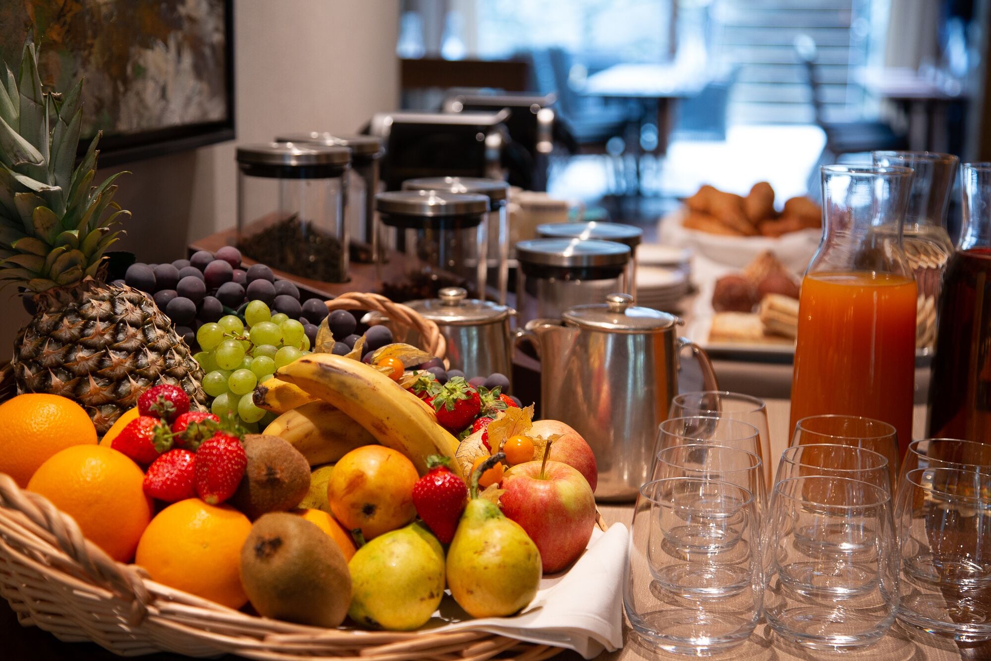 Un buffet de petit-déjeuner proposant une variété de fruits, une carafe de jus d’orange et plusieurs verres vides.