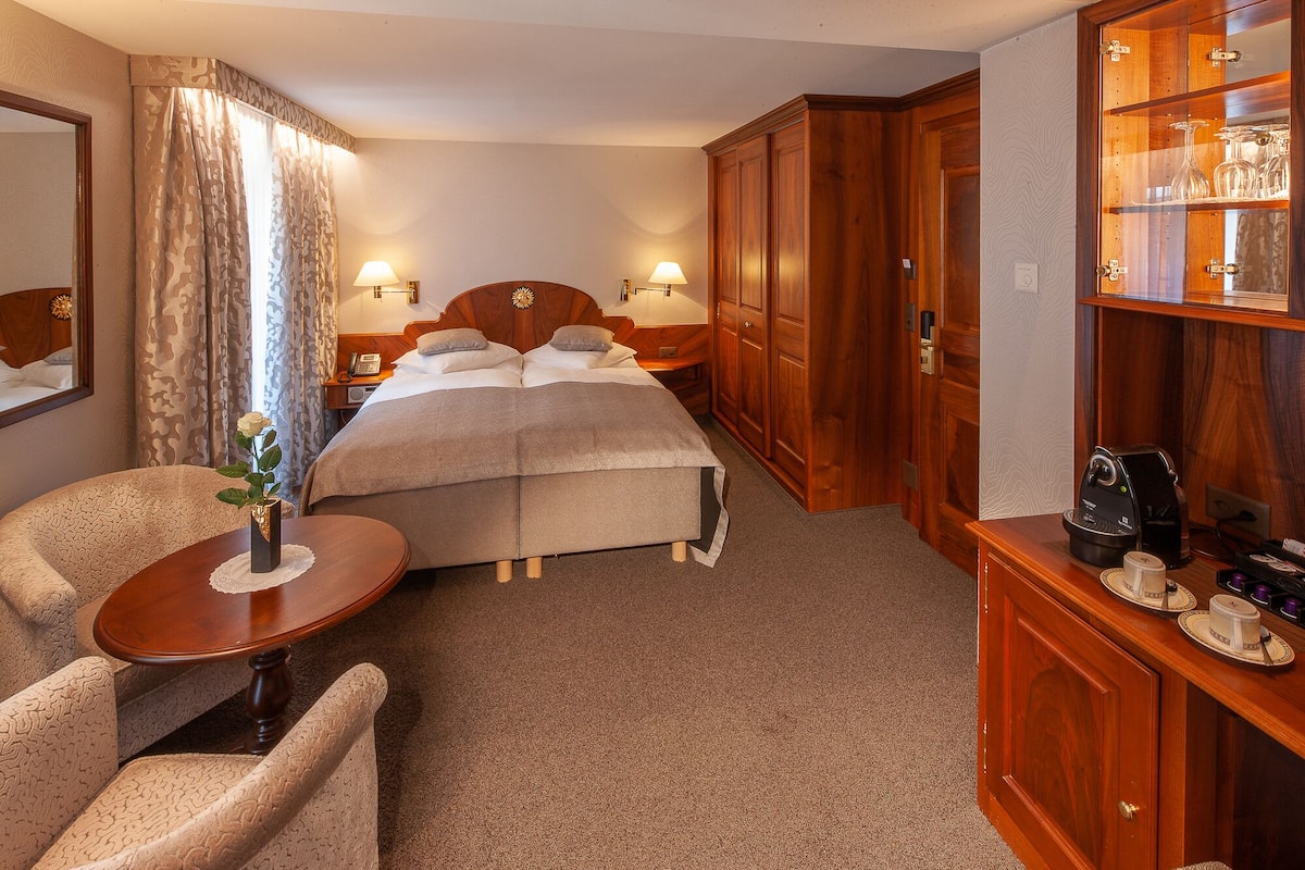 Een hotelkamer met een bed, nachtkastjes, een bureau, een stoel, een kledingkast en een minibar.