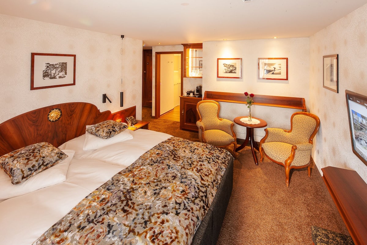 Een hotelkamer met een groot bed, twee fauteuils, een tafeltje en beelden in lijsten aan de muur.