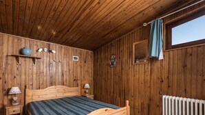 Ett sovrum med träpanel på väggarna, en säng i trä, sänglampor, ett element och ett fönster med gardin.