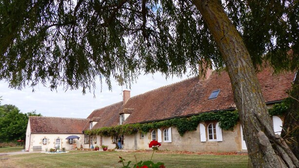 Un bâtiment traditionnel en pierre, doté d’un toit en tuiles, entouré d’une pelouse bien entretenue et de plantes en fleurs.