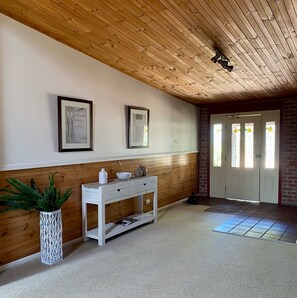 A hallway with a wooden ceiling, a white console table with decorative items, and a door with stained glass windows. - Bluebush Estate - The Lodge (Rothbury)