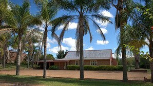 A house with a brick exterior, surrounded by a well-maintained lawn and palm trees. - Bluebush Estate - The Lodge (Rothbury)