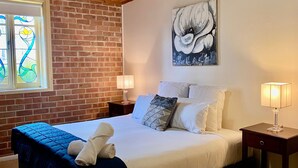 A bedroom with a bed, two bedside tables, a ceiling fan, a stained glass window, and a painting on the wall. - Bluebush Estate - The Lodge (Rothbury)