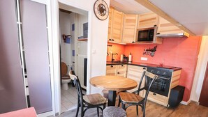 Eine kleine Küche mit Holzschränken, einer Mikrowelle und einem Herd. Es gibt einen Esstisch mit Stühlen und einen kleinen Hocker.