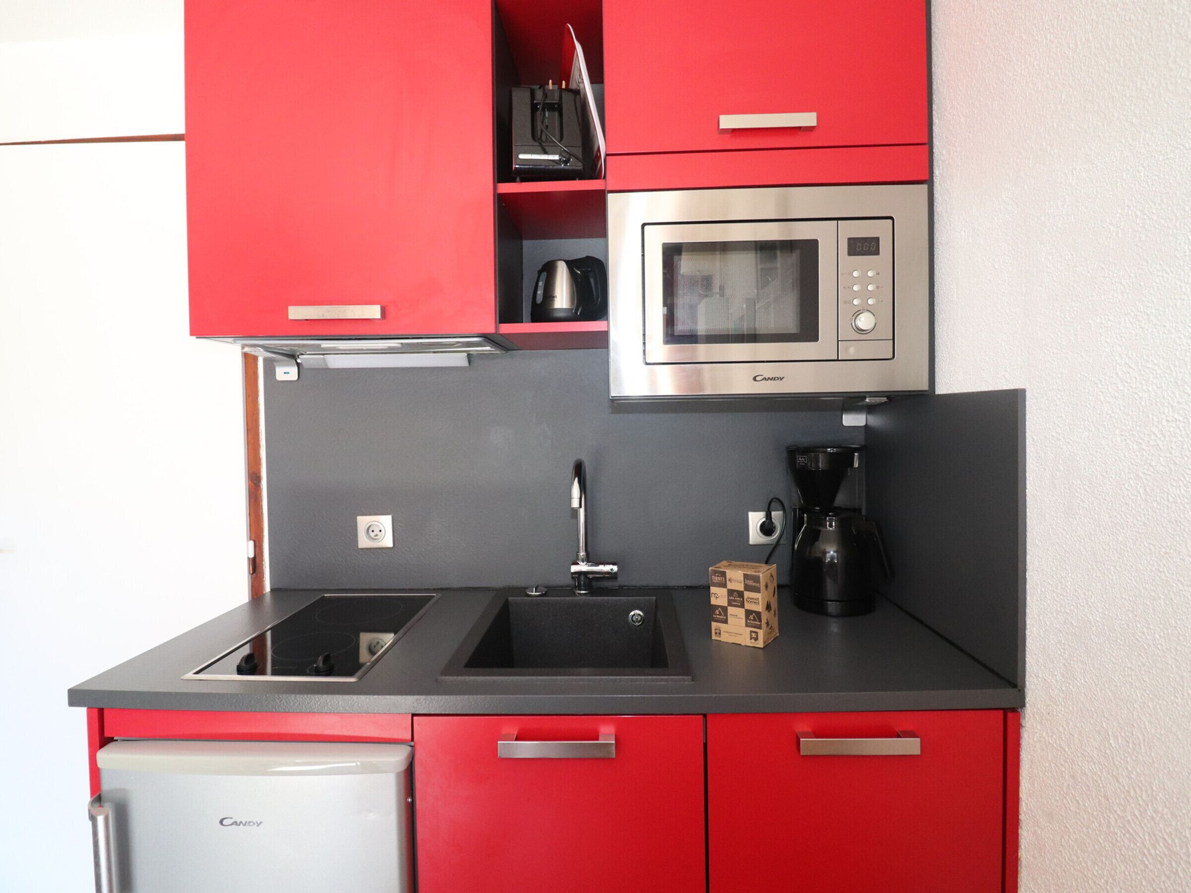 A compact kitchen with red cabinets, a stainless steel microwave, a coffee maker, and a refrigerator.