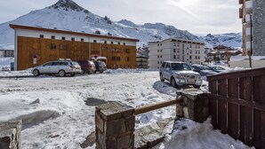 Un parking enneigé où sont garées plusieurs voitures, un bâtiment en bois et une montagne en arrière-plan.