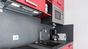 Une cuisine moderne dotée d’un plan de travail noir, de placards rouges, d’un four à micro-ondes encastré, d’une machine à café et d’un évier à deux bacs.