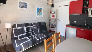 Un espace de vie compact comprenant un canapé, une table à manger, un coin cuisine et un téléviseur fixé au mur.