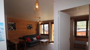 Una habitación acogedora con pared de madera, un sofá, una mesa y una ventana con vistas a edificios y montañas.