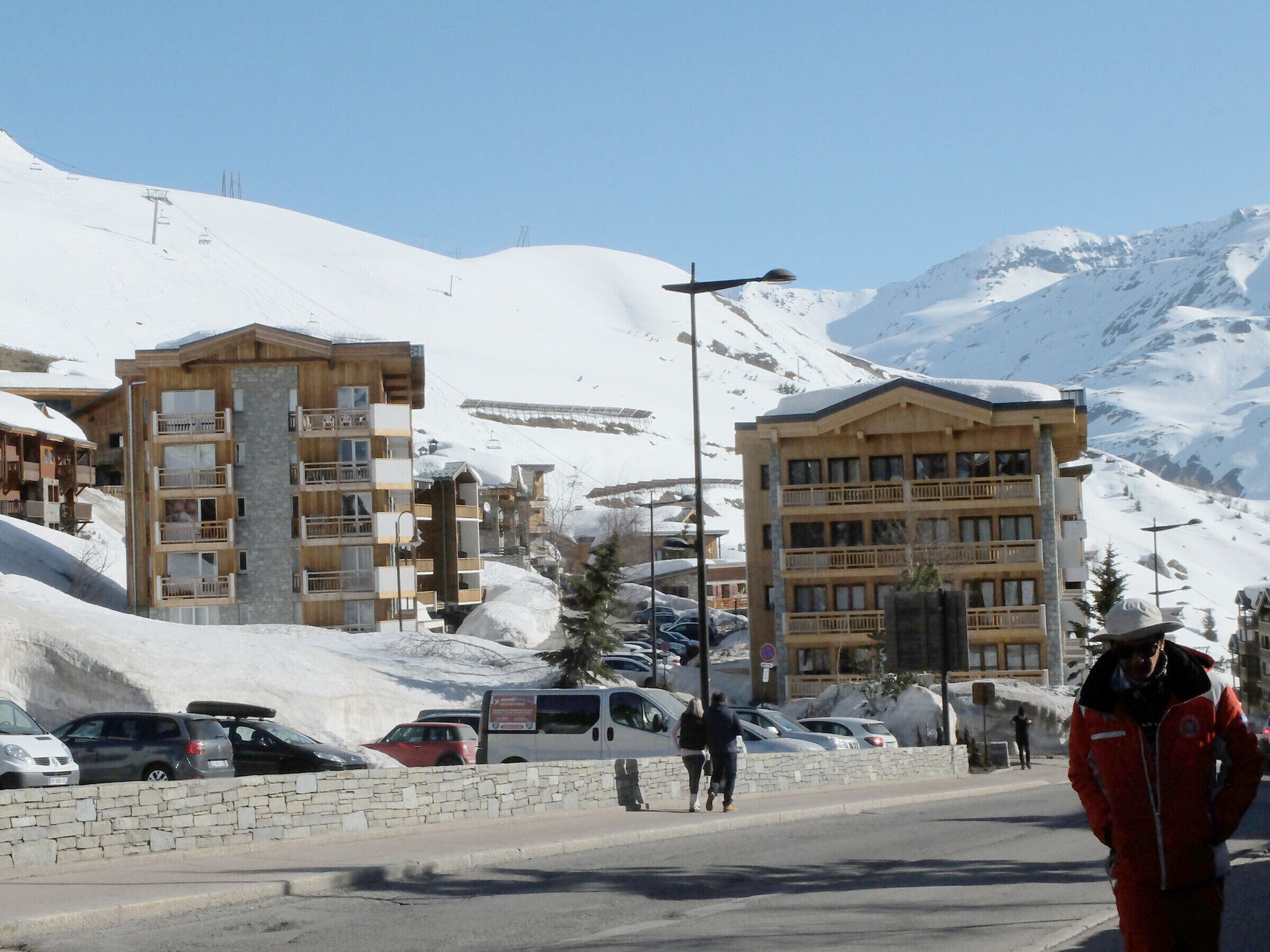 A snow-covered mountain town with multi-story buildings, a paved road, and parked cars.