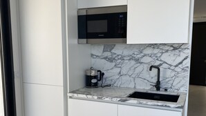Eine kompakte Küche mit weißen Schränken, einer schwarzen Mikrowelle, einer Marmor-Spritzschutzwand und einem Spülbecken mit Armatur.