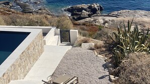 Ein Poolbereich mit Blick auf das Meer, umgeben von Felsen und trockener Vegetation.