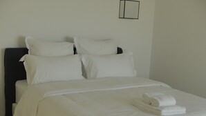 Ein ordentlich bezogenes Bett mit weißen Leinen und aufgerollten Handtüchern, ein dunkles Kopfstück und ein kleines gerahmtes Bild an der Wand.