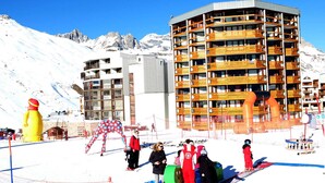 A ski resort with a multi-story building, ski lifts, and a snowy mountain backdrop.
