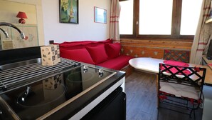 A compact kitchen with a stove, sink, and a red sofa. There is a window with curtains and a wall-mounted picture. - Practical studio at the foot of slopes - Pets allowed (Tignes)