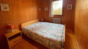 Puinen huone, jossa on sänky, yöpöytä, lamppu ja ikkuna, josta avautuu näkymä vehreään maisemaan.