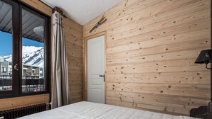 A bedroom with a wooden wall, a window with a view of snow-capped mountains, a bed, and a door.
