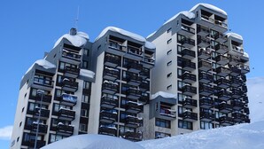 A multi-story hotel with balconies and a ski slope in the background.