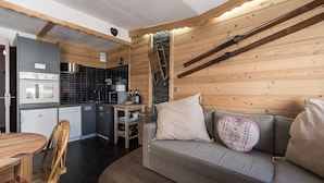 A compact living space with a kitchenette, a sofa with a heart-shaped pillow, and a wooden dining table.
