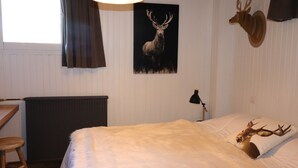 Un dormitorio con una cama grande, un escritorio de madera, un radiador, una lámpara y decoraciones de cabeza de ciervo en la pared.