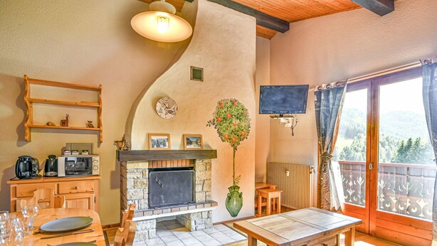 Ein gemütliches Wohnzimmer mit Kamin, Holzmöbeln, einem Fernseher und einem Balkon mit schöner Aussicht.