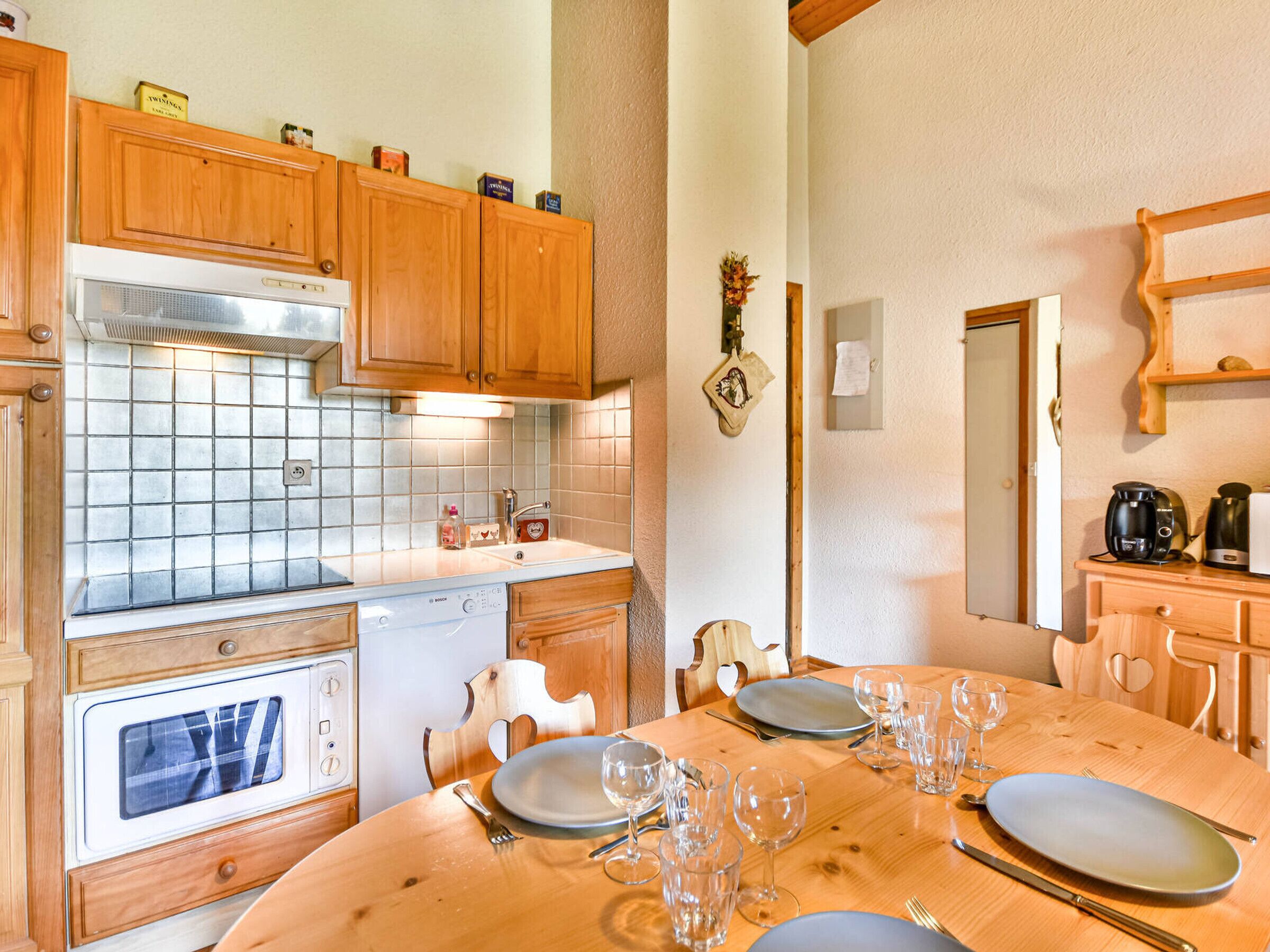 A kitchen with wooden cabinets, a tiled backsplash, a Bosch dishwasher, and a dining table set for six.