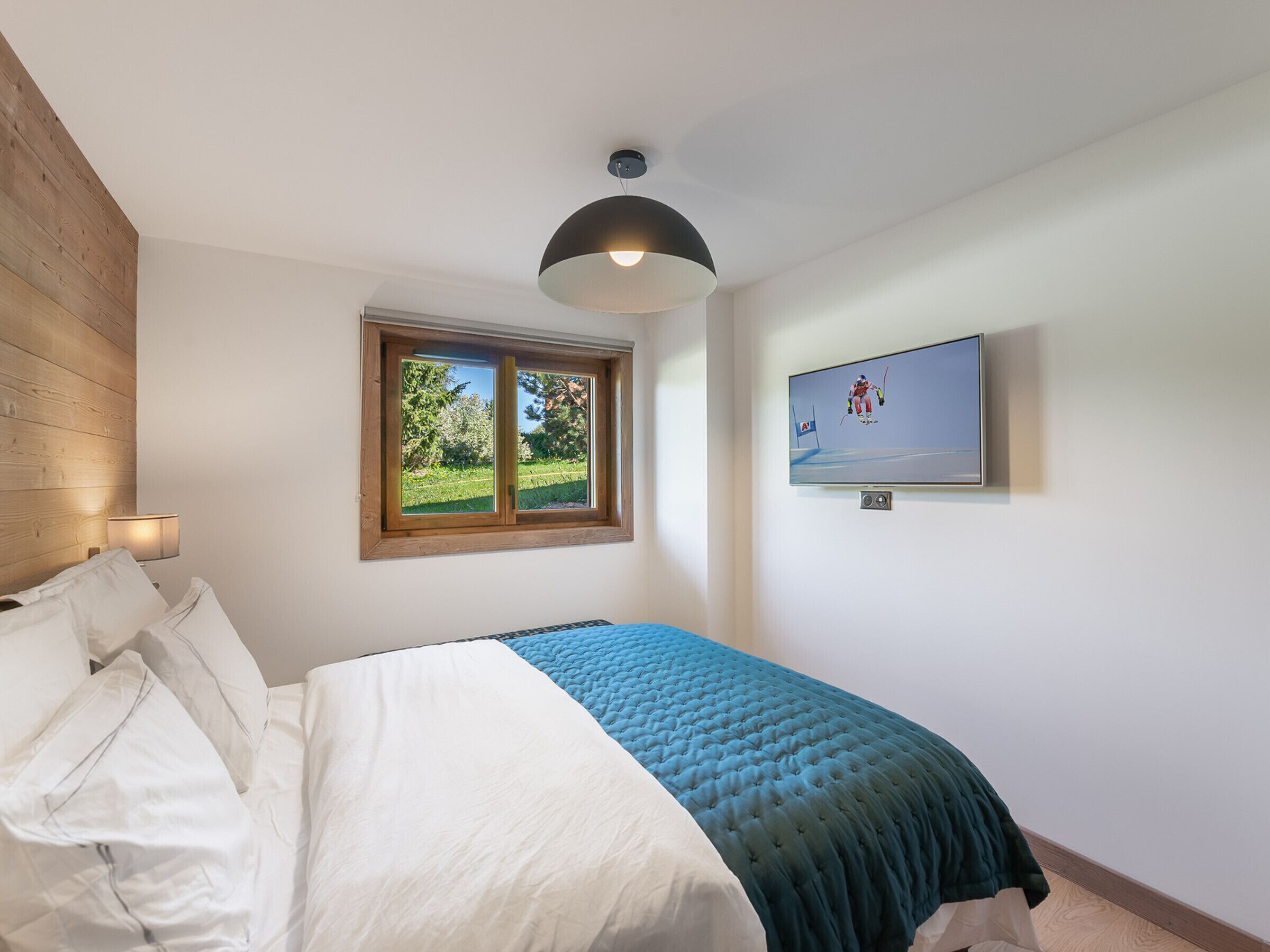 A bedroom with a bed, a window, a television, and a ceiling light.
