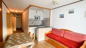A compact living space with a kitchenette, a dining area, and a red sofa.