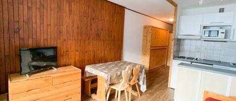Een compacte keuken met houten kastjes, een magnetron en een kleine eettafel met stoelen.