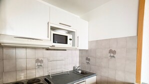 A compact kitchen with white cabinets, a microwave, a stove, and a sink.