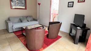 Ein Wohnzimmer mit grauem Sofa, einem Couchtisch, zwei braunen Sesseln, einem Fernsehgerät auf einem Schrank und einem Fenster mit Vorhängen.