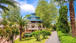 Ein Gebäude im traditionellen Stil mit blauem Dach, umgeben von üppiger Vegetation und Palmen.