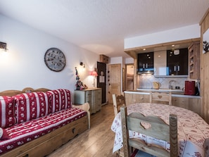 Ein gemütliches Zimmer mit einer Holzsofa, einem kleinen Esstisch, einer Küchenzeile mit Holdekor und einer Wanduhr.