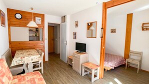 A small, cozy room with a wooden dining table, a TV, a bed, and a chair.