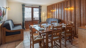 A cozy dining area with a wooden table set for four, surrounded by wooden chairs. A cushioned bench is against the wall, and a window offers a view of a snowy landscape. - Charming 56m2 apartment for 6 with balcony and parking - Val Thorens (Val Thorens)