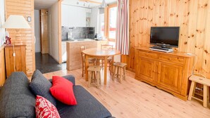 A cozy living room with a sofa, TV, wooden cabinets, and a dining area.