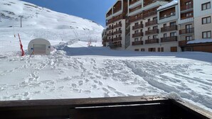 A snow-covered ski slope with a building featuring multiple balconies and a ski lift in the background.