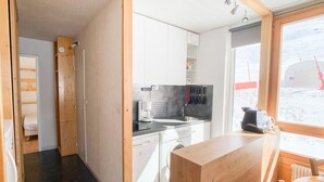 A compact kitchen with a sink, stove, and white cabinets. A wooden counter and a dining table with chairs are visible.