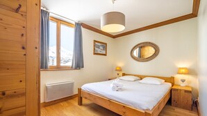 A wooden-framed bedroom with a bed, two bedside lamps, a window with curtains, a radiator, and a mirror on the wall. - Renovated ski-in ski-out apartment, balcony, WIFI, 4 bedrooms (Tignes)