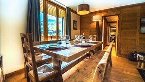 A wooden dining table set with plates, glasses, and a bottle, with a view of mountains through large windows. - Renovated ski-in ski-out apartment, balcony, WIFI, 4 bedrooms (Tignes)