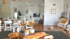 Ein Esstisch mit einem Baguette, zwei Weingläsern, einer Weinflasche, einer Nussmischung und einer Kerze.