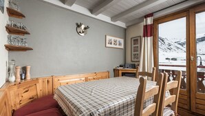 Ein gemütliches Zimmer mit einem hölzernen Bett, einem Esstisch mit Stühlen, einem kleinen Schreibtisch und einem Fenster mit Blick auf eine verschneite Landschaft.