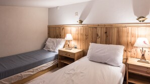 Ein Zimmer mit zwei Einzelbetten, Holz-Kopfteilen, Nachttischen mit Lampen und einer schlichten weißen Wand.