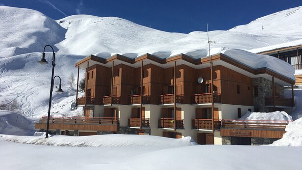 Ein mehrstöckiges Holzgebäude mit Balkonen, umgeben von schneebedeckten Bergen.