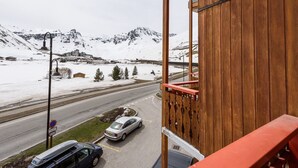 Blick von einem Balkon auf eine verschneite Landschaft mit Bergen, einer Straße und abgestellten Autos.