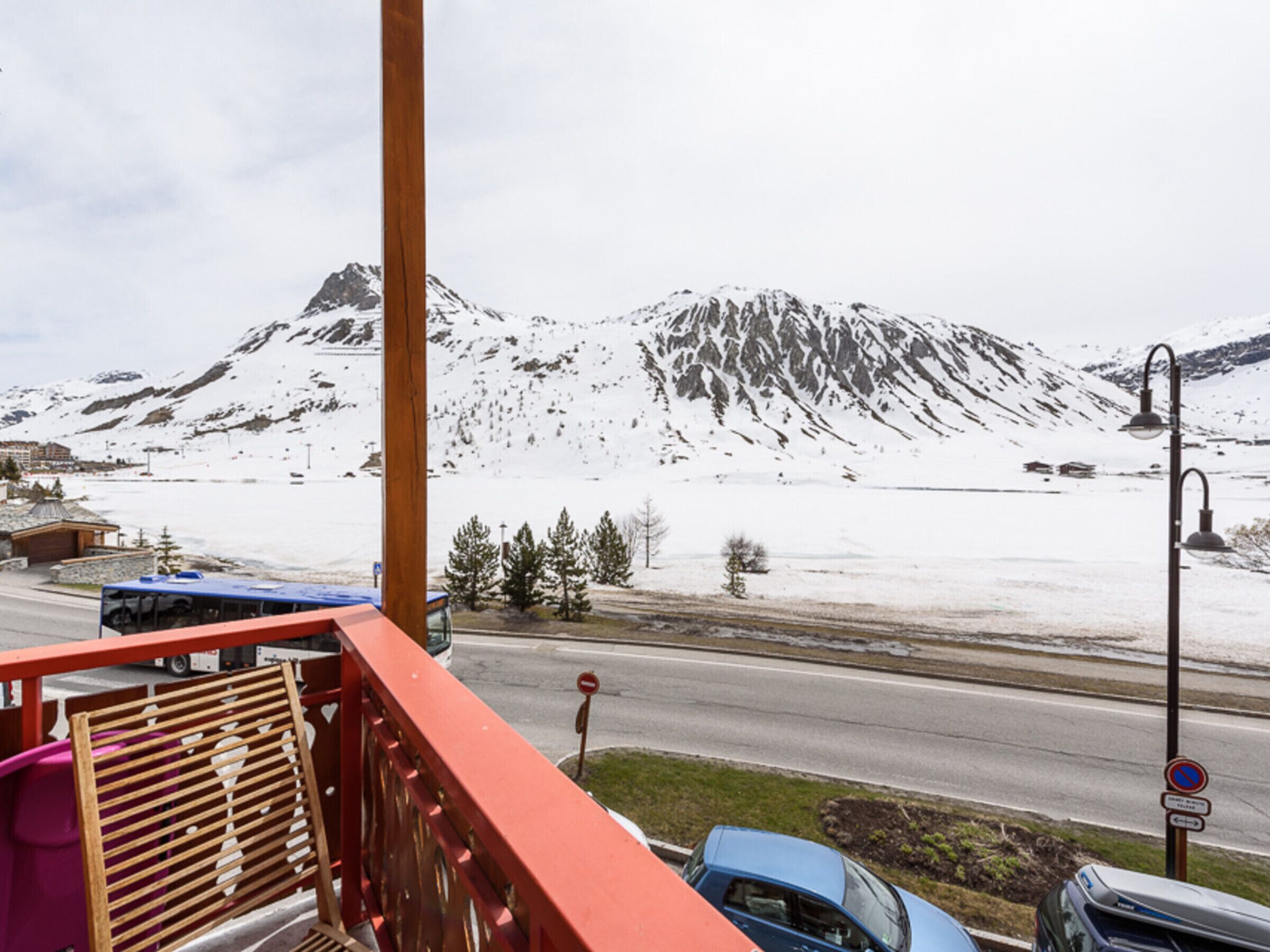Un balcó amb vista a una muntanya plena de neu, una carretera amb vehicles i un fanal.